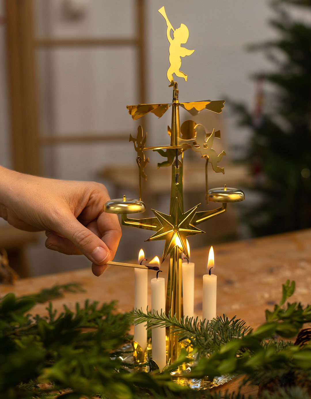 En hand str&auml;cker t&auml;nder ljusen i ett &auml;nglaspel i m&auml;ssing