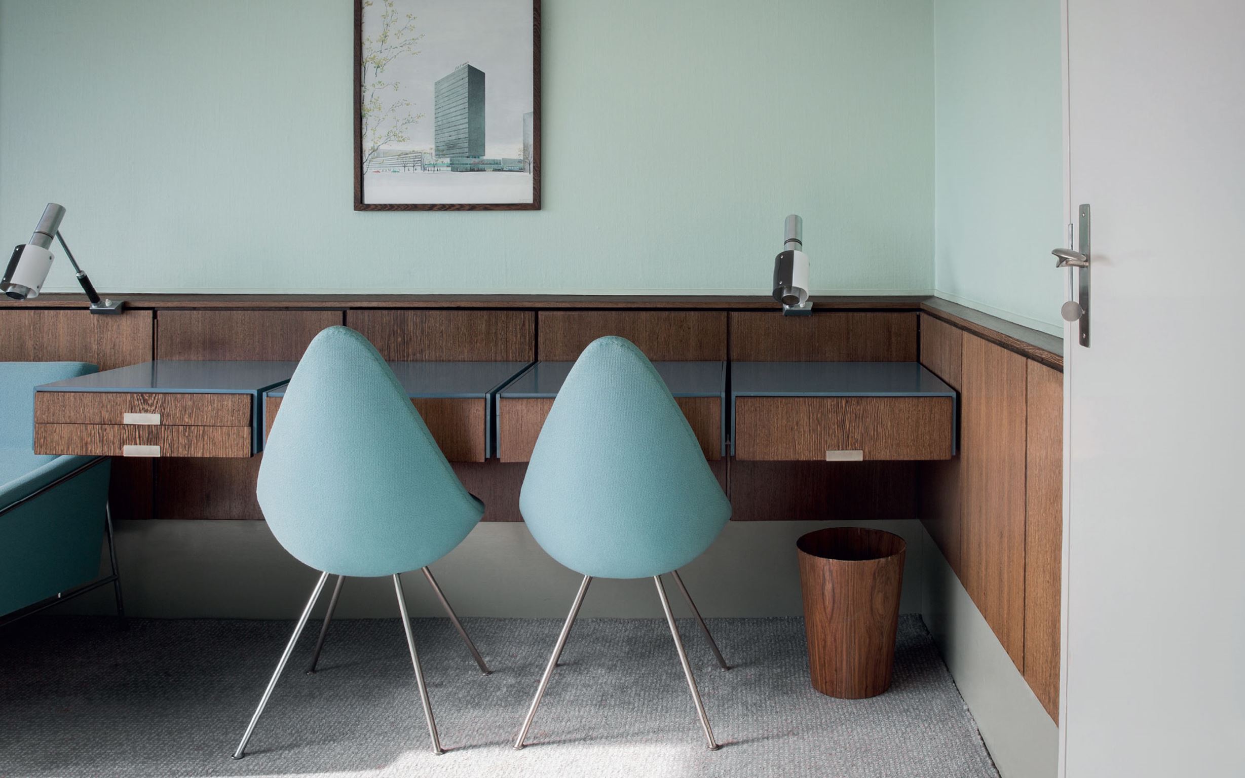 Skrivbordssektion med skrivbord i m&ouml;rkbrunt tr&auml; tillsammans med kl&auml;dda, turkosa, stolar i 50-talsstil.