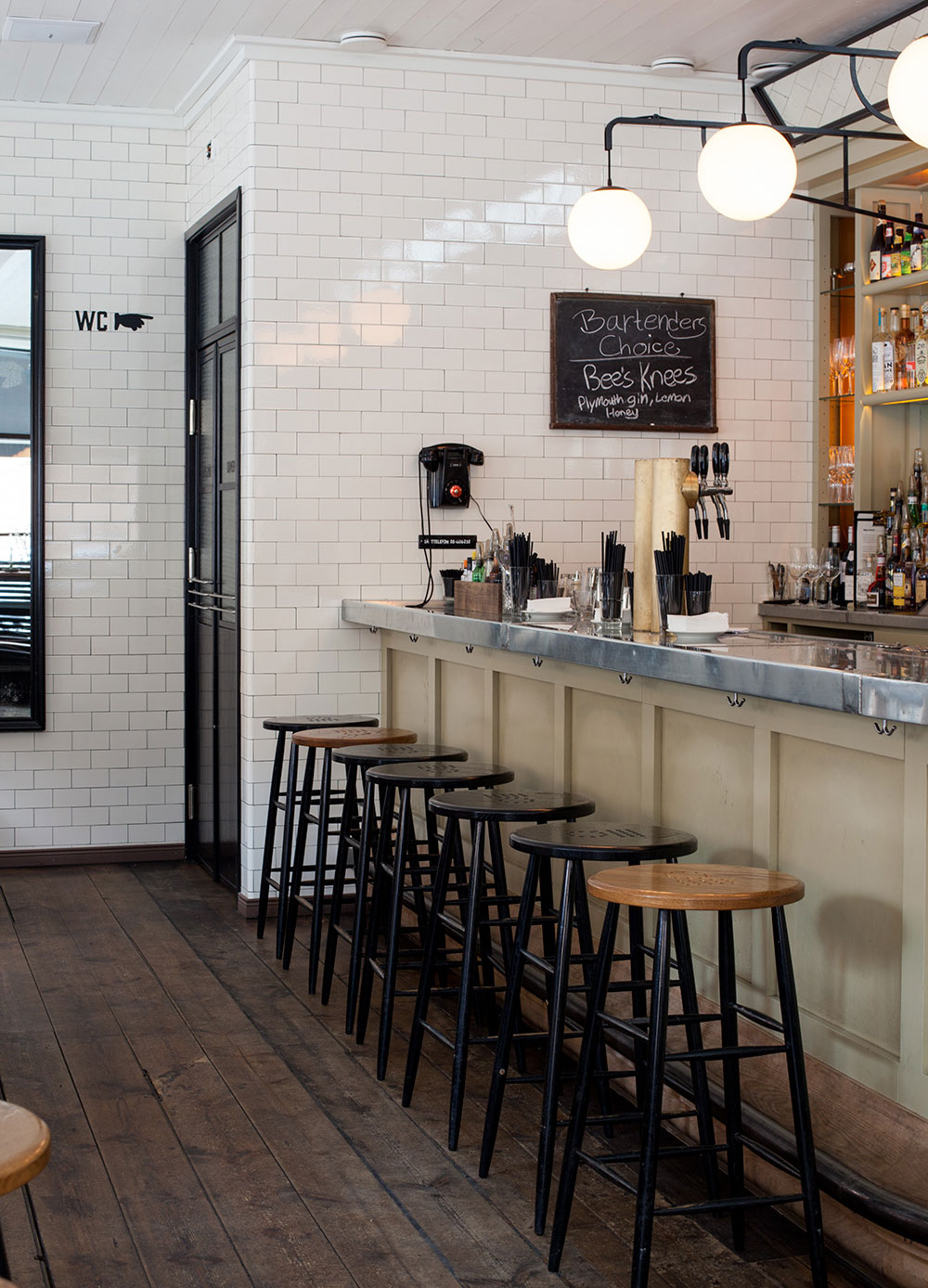 Bardel med h&ouml;ga pallar och kaklade v&auml;ggar i vitt h&ouml;gblankt kakel.