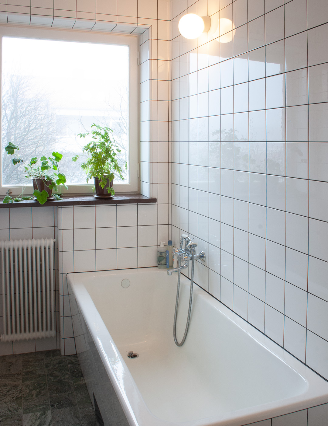 Funkisbadrum med inbyggt badkar med vitt kakel i raka f&ouml;rband.