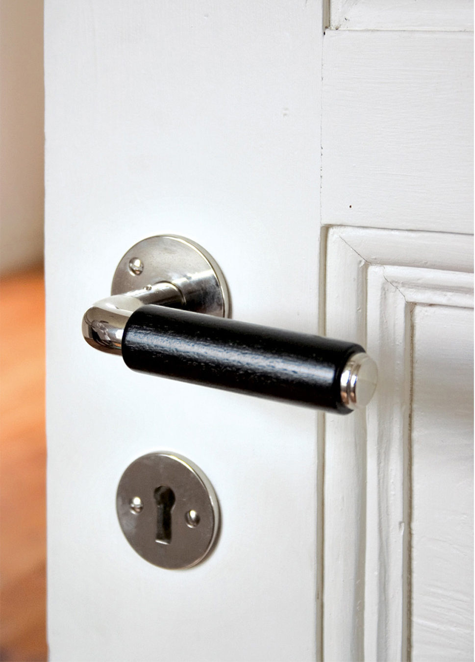 Ett funkishandtag med svart grepp i tr&auml; med profilerad &auml;ndknopp i f&ouml;rnicklad m&auml;ssing p&aring; ett vit spegeld&ouml;rr.