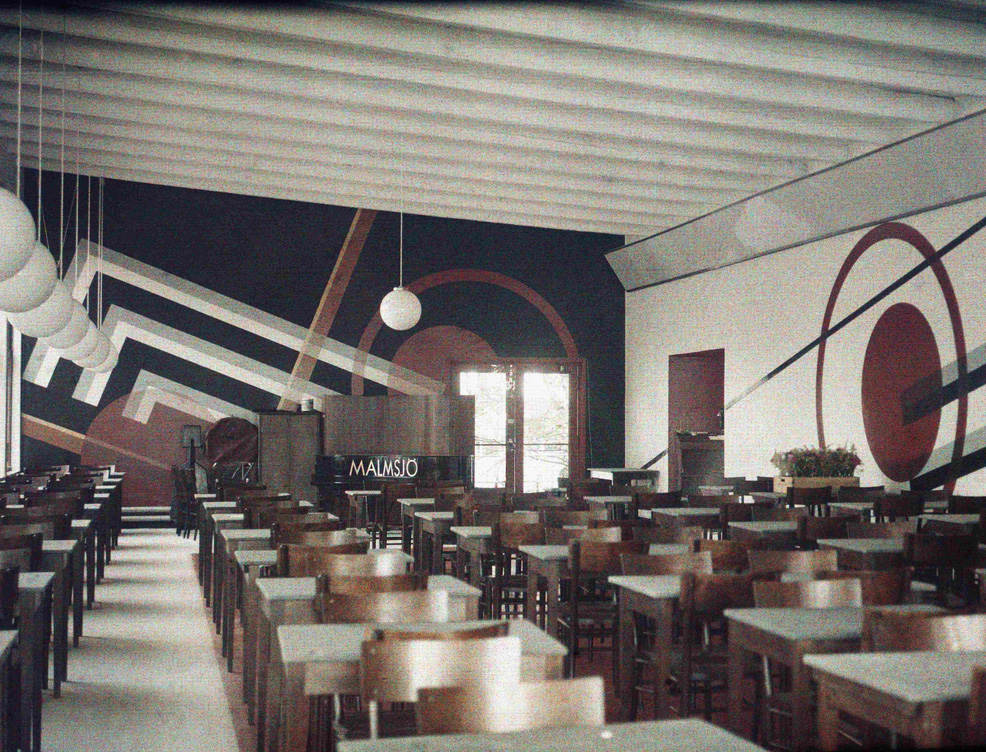 Matsal i funktionalistisk anda med stolar i m&ouml;rkt tr&auml; och v&auml;ggm&aring;lningar med geometriska motiv.