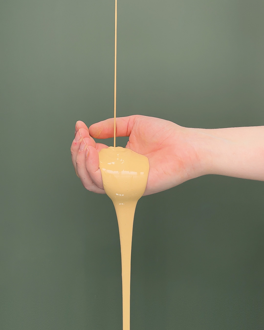 Ljusgul f&auml;rg rinner ner i en &ouml;ppen hand mot en m&ouml;rkgr&ouml;n bakgrund.