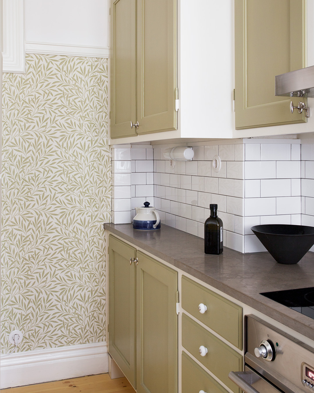 Beslag av porslin p&aring; l&aring;dor och f&ouml;rnicklade vred p&aring; luckor i ett k&ouml;k m&aring;lat med linoljef&auml;rg i kul&ouml;ren Ljus Oliv.