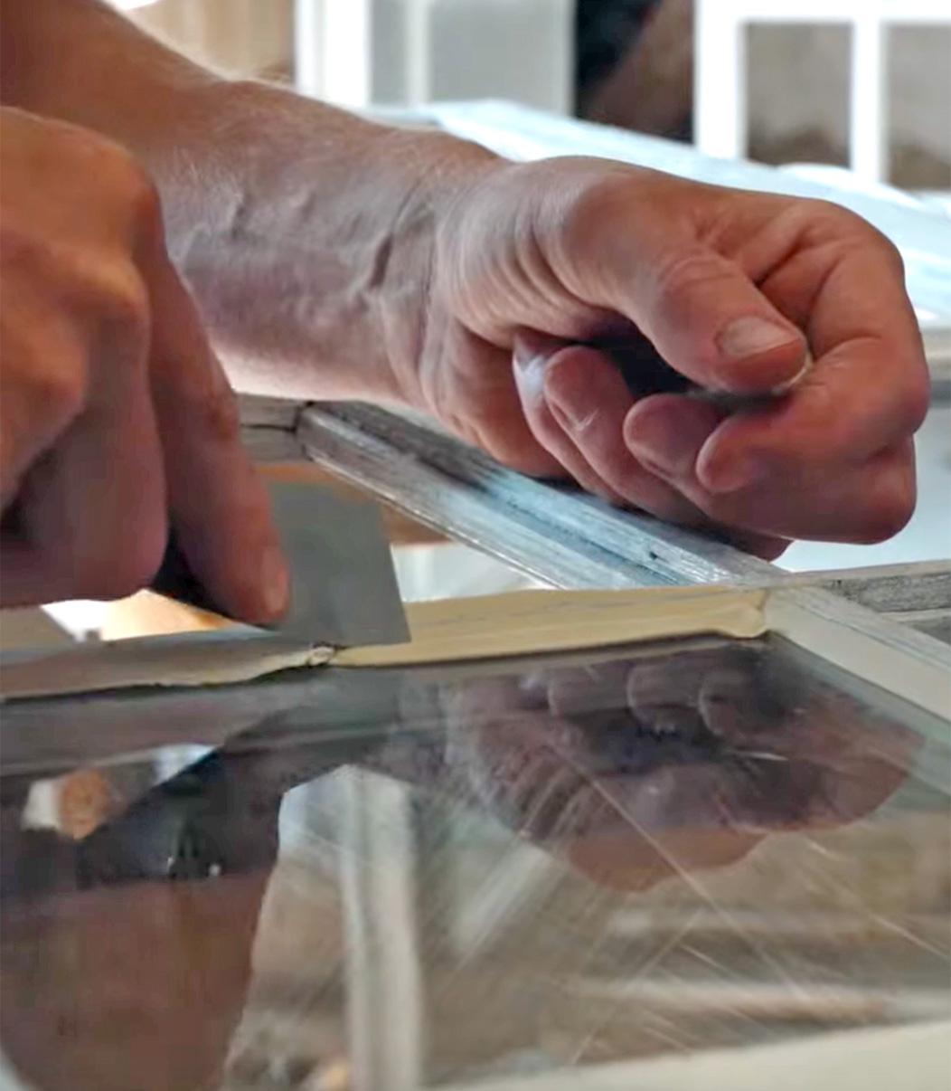 Tv&aring; h&auml;nder i bild l&auml;gger nytt kitt p&aring; spr&ouml;jsat f&ouml;nster.