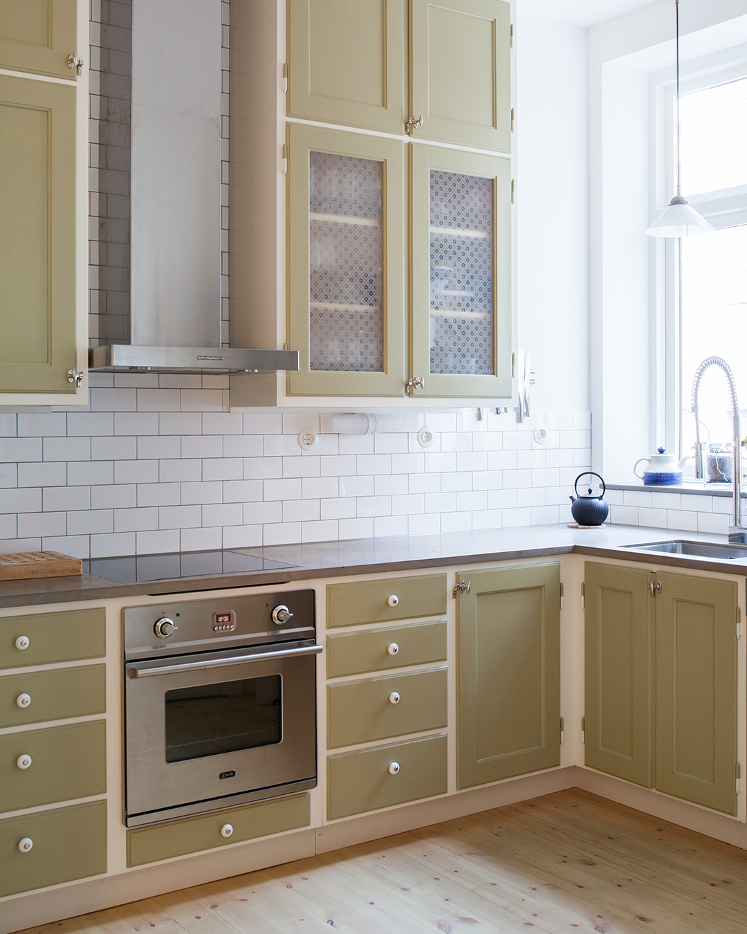 Beslag av porslin p&aring; l&aring;dor och f&ouml;rnicklade vred p&aring; luckor i ett k&ouml;k m&aring;lat med linoljef&auml;rg i kul&ouml;ren Ljus Oliv.