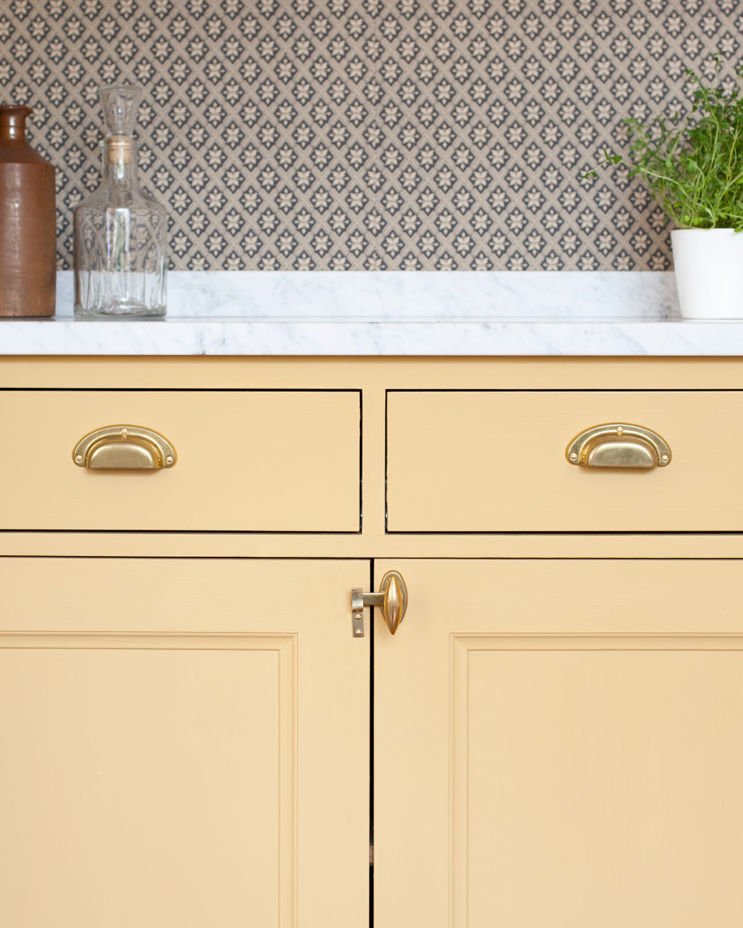 Beslag i obehandlad m&auml;ssing p&aring; sk&aring;p och l&aring;dor i ett k&ouml;k m&aring;lat med linoljef&auml;rg i kul&ouml;ren Varmgul.