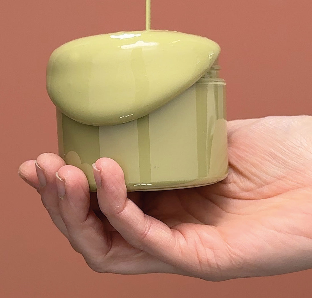 en hand h&aring;ller en burk pistagegr&ouml;n f&auml;rg mot en r&ouml;d bakgrund