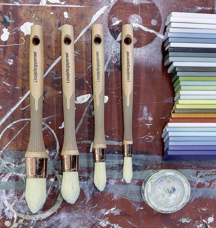 Linoljef&auml;rgspenslar och provbitar p&aring; en arbetsb&auml;nk med f&auml;rgfl&auml;ckar.