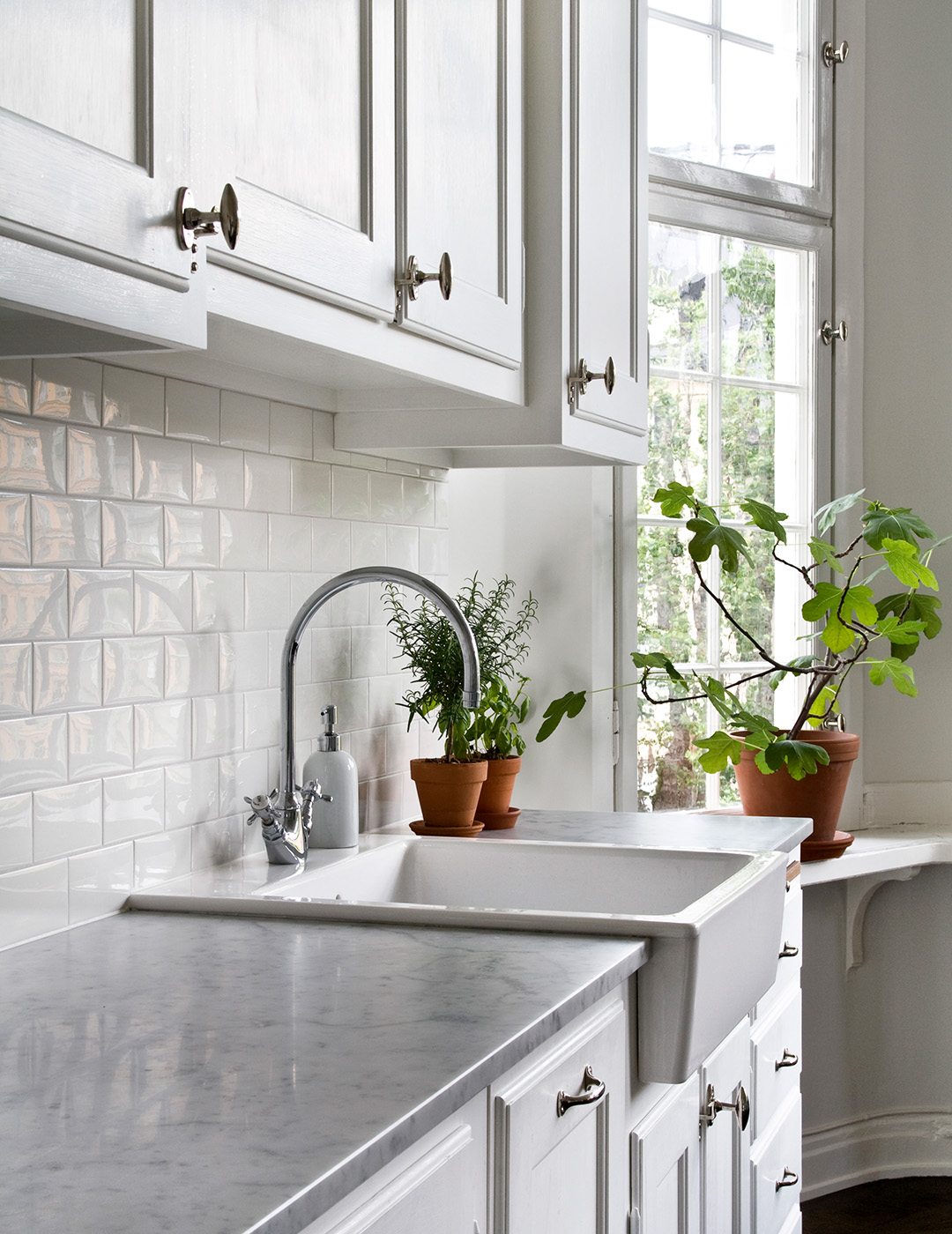 Ett vitt k&ouml;k i sekelskiftesstil, f&ouml;rnicklade beslag och kryddv&auml;xter med krukv&auml;xter i f&ouml;nstret i bakgrunden.