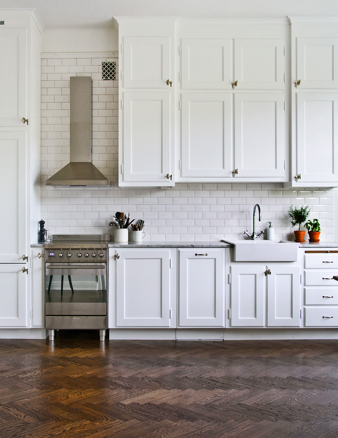 Ett vitt k&ouml;k i sekelskiftesstil i bakgrunden. Ett brunbetsat golv av fiskbensparkett.