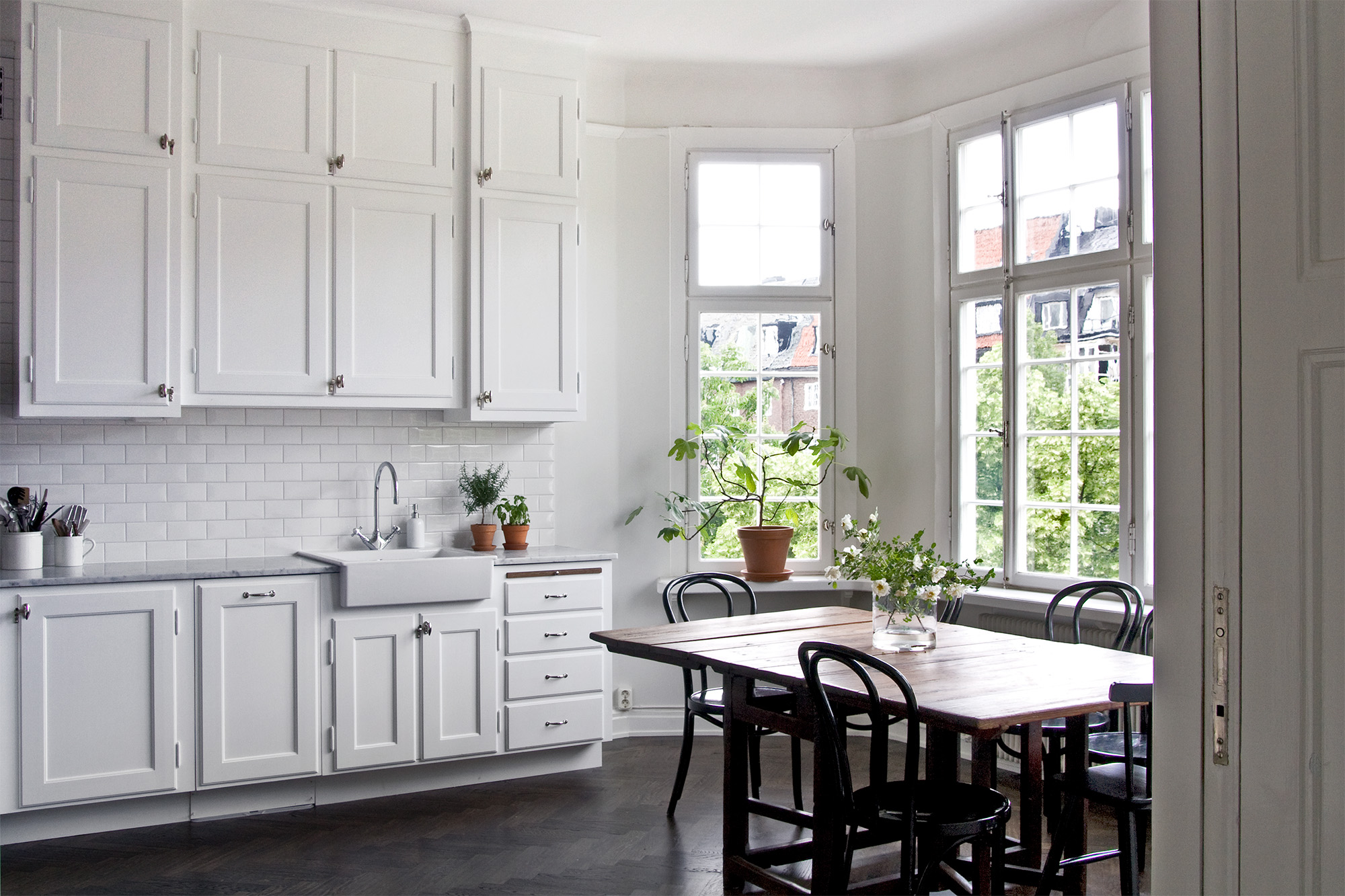 Sekelskiftesk&ouml;k med m&aring;ttbyggd k&ouml;ksinredning m&aring;lad med vit linoljef&auml;rg. Matbord i m&ouml;rkt tr&auml;.