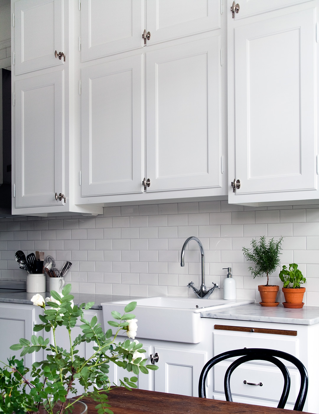 Ett vitt k&ouml;k i sekelskiftesstil, f&ouml;rnicklade beslag och kryddv&auml;xter med ett matbord i f&ouml;rgrunden.