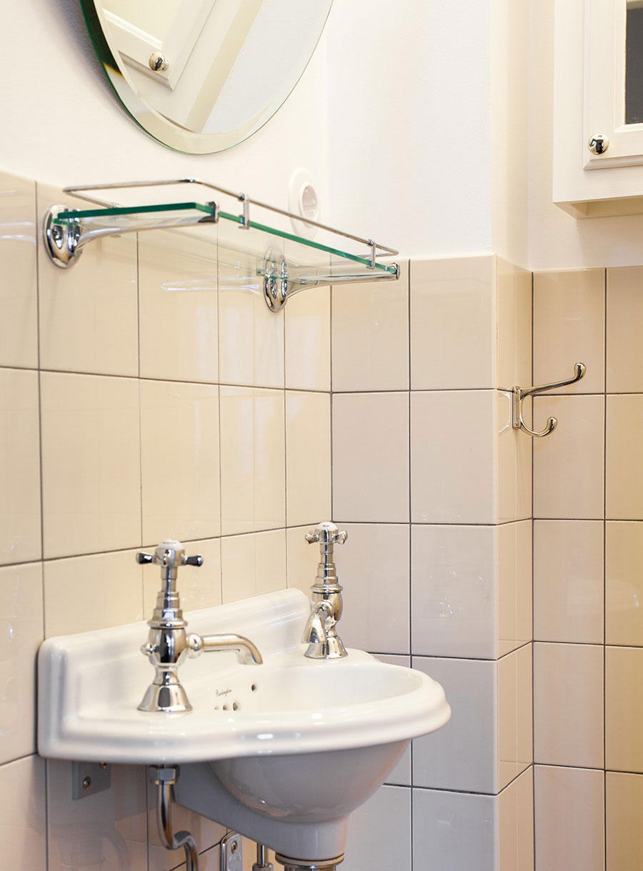 Handfat p&aring; g&auml;sttoalett med cremef&auml;rgade, halvkaklade v&auml;ggar.