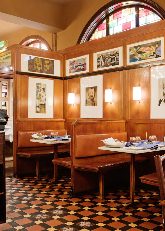 Restaurangdel med bruna l&auml;ders&auml;ten, vita dukar och ett m&ouml;nstrat klinkergolv.