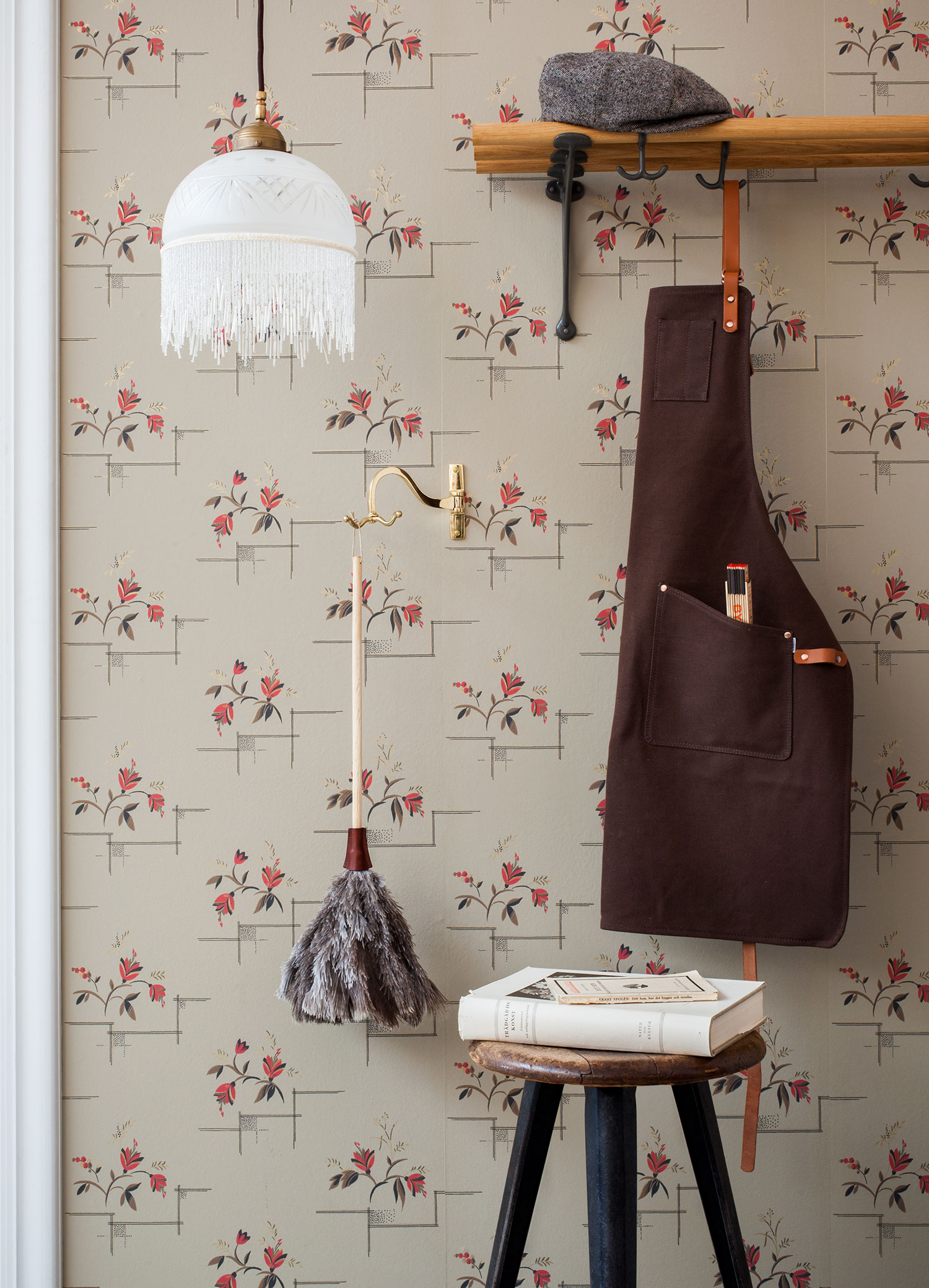 Tapetserad v&auml;gg med 20-talshatthylla och p&auml;rlfranslampa