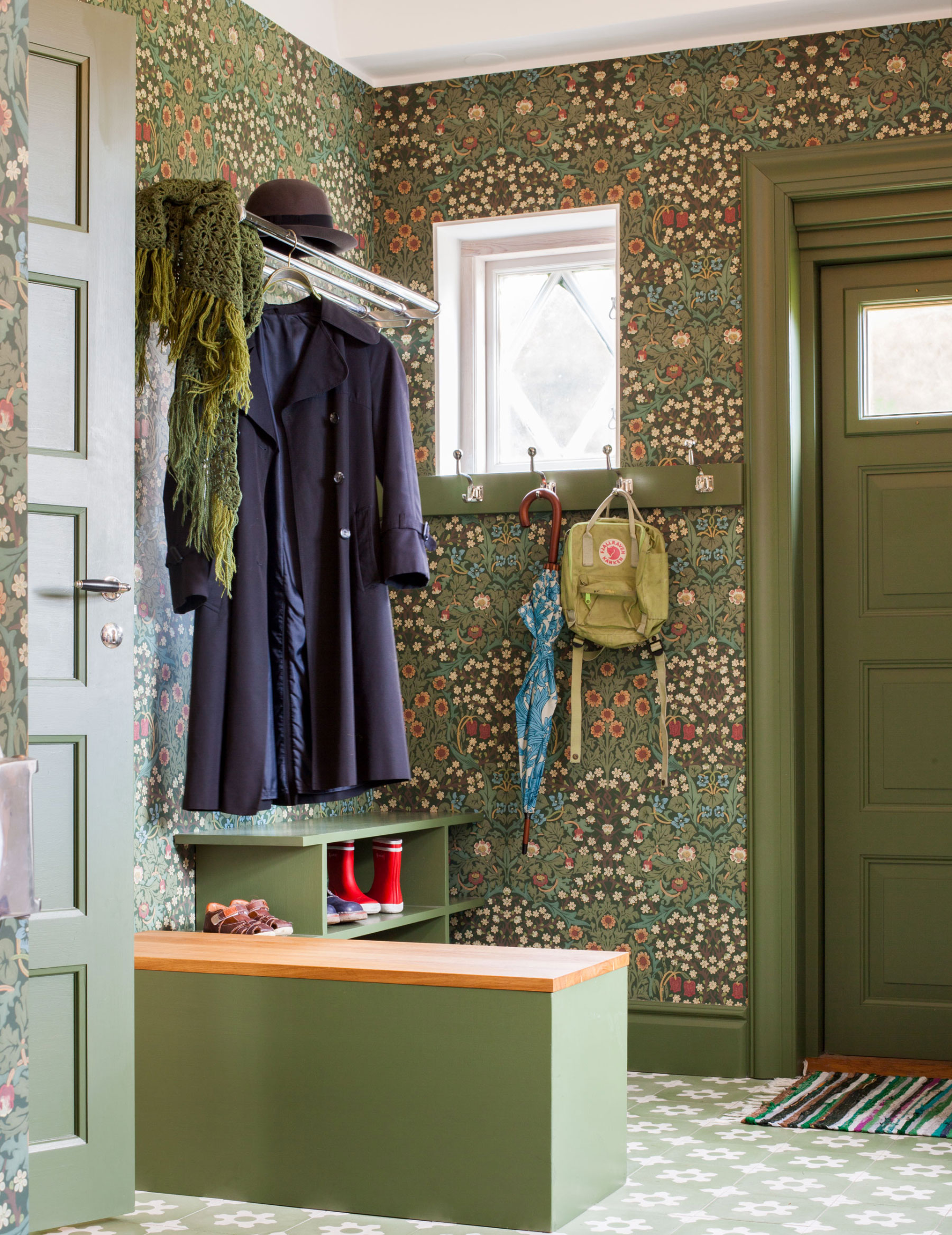 Tapetserad 20-talshall i gr&ouml;na toner med kl&auml;dkrokar i f&ouml;rnicklad m&auml;ssing