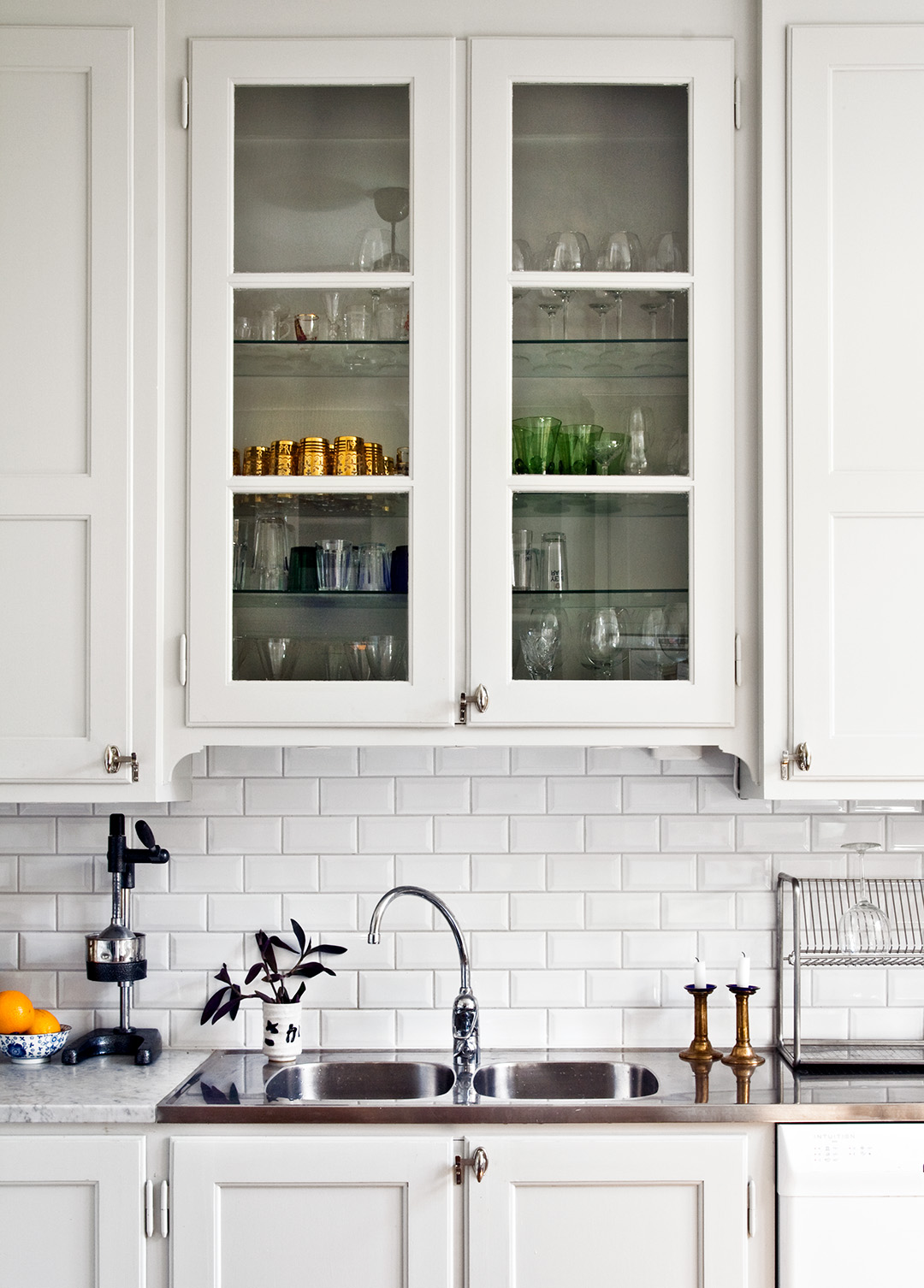 Sektion av m&aring;ttbyggt k&ouml;k i vitt med glasade k&ouml;ksluckor och sk&aring;psvred i f&ouml;rnicklad m&auml;ssing.